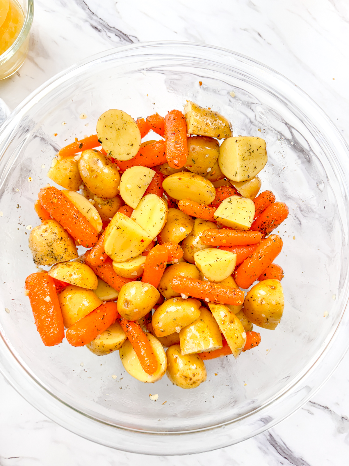 A top view of carrots and potatoes in a glass bowl.