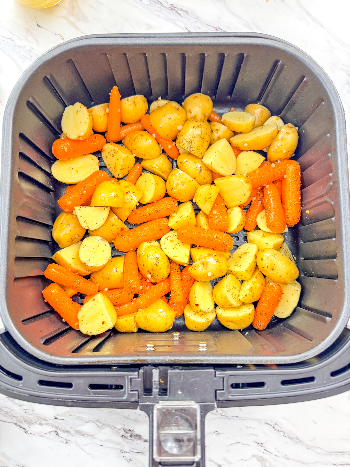 A top view of carrots and potatoes in an air fryer basket.