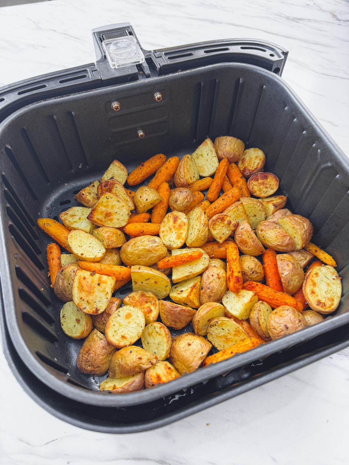 A side view of carrots and potatoes in an air fryer basket.