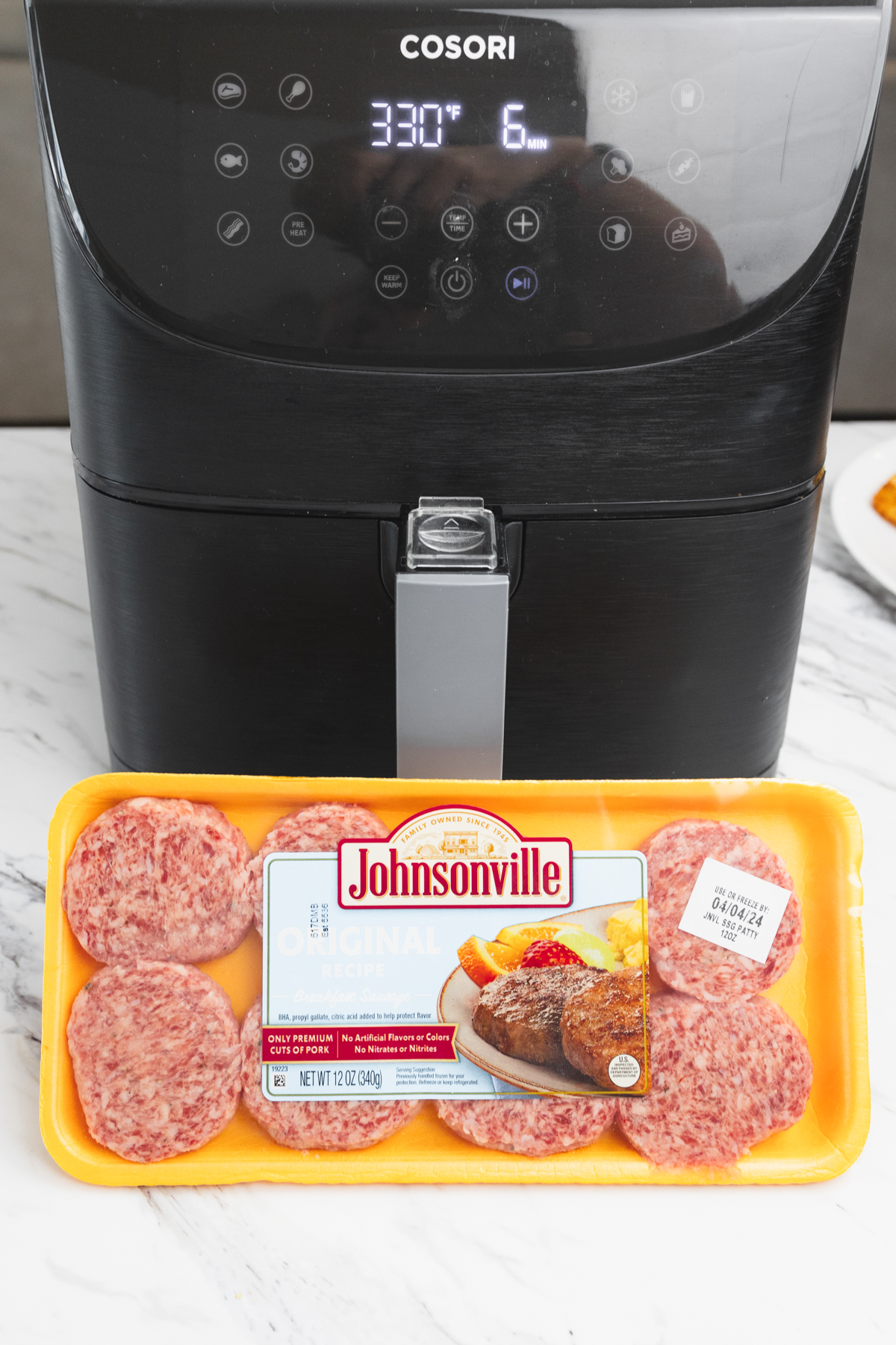 Close up of a pack of fresh sausage patties in front of an air fryer.