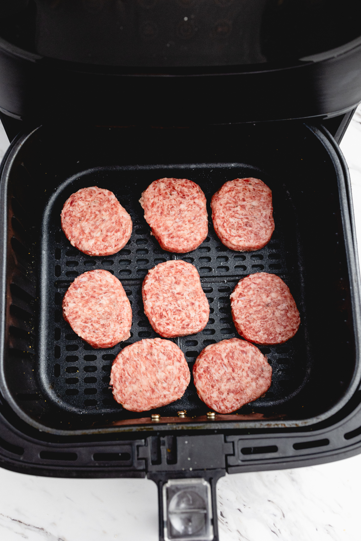 Top view of fresh sausage patties in the basket of an open air fryer.