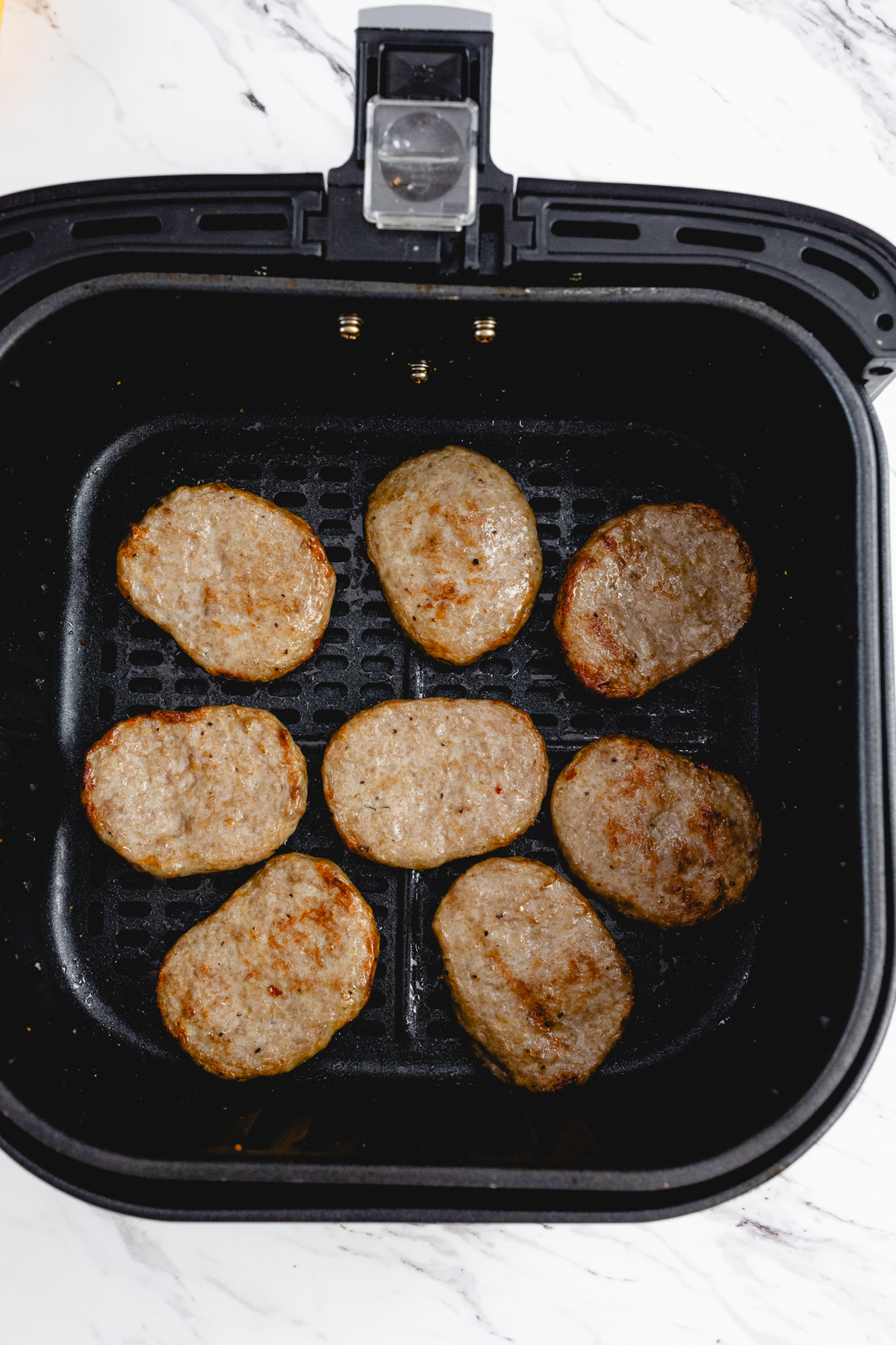 Top view of cooked sausage patties in the basket of an open air fryer.