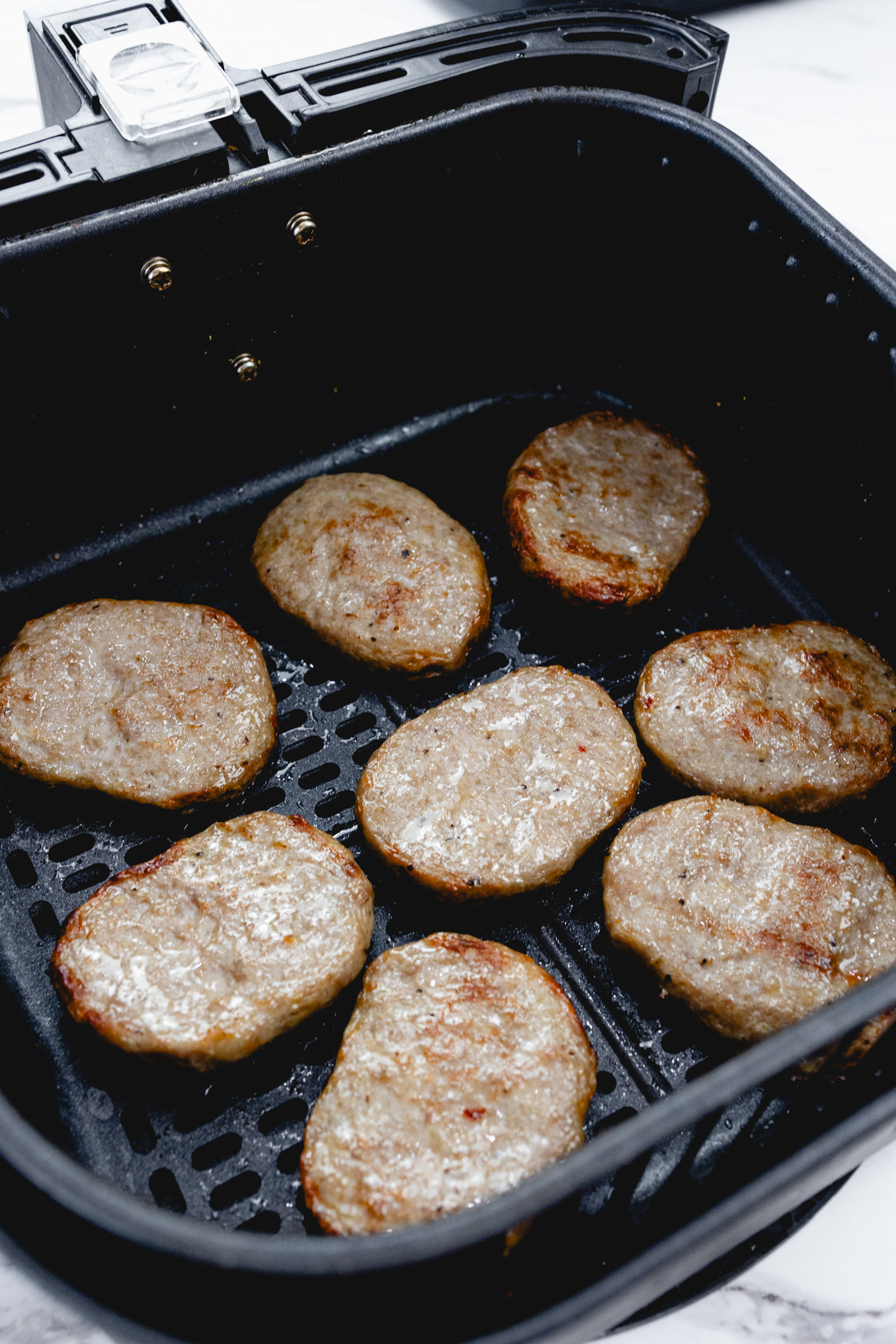 Close up of cooked sausage patties in the basket of an open air fryer.