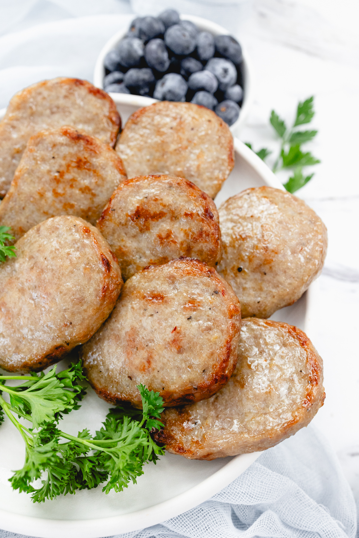 Close up of cooked sausage patties on a white plate with a leafy green garnish to the side.