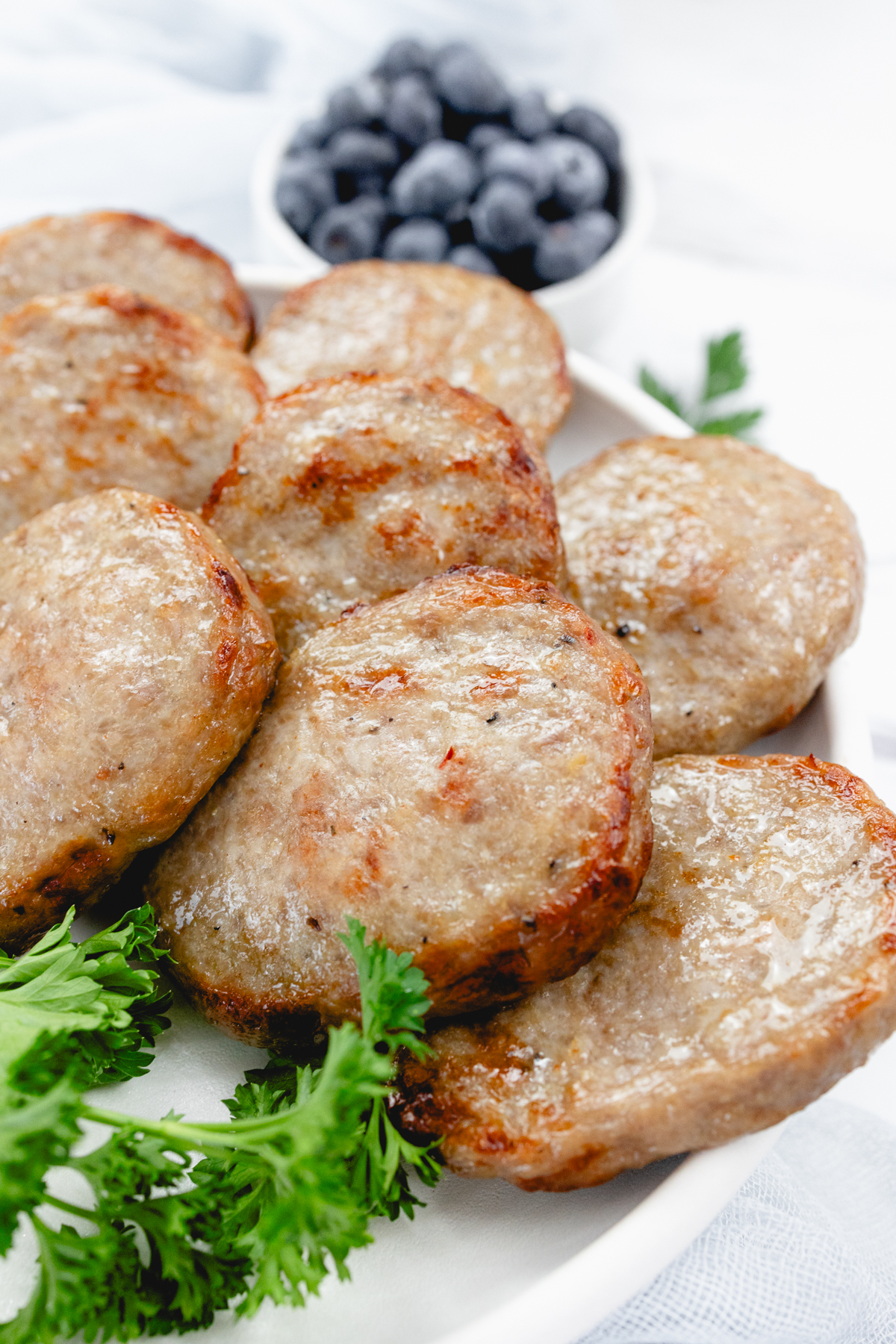 Close up of cooked sausage patties on a white plate with a leafy green garnish to the side.