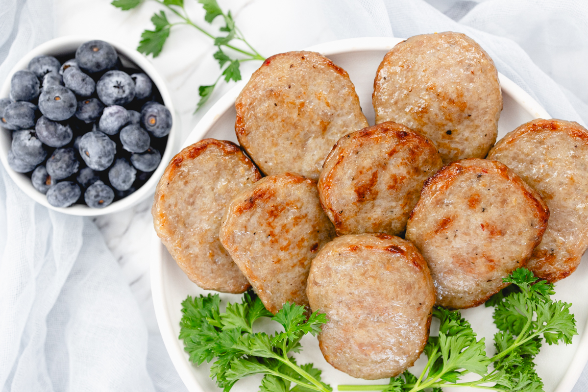 Top view of cooked sausage patties on a white plate with a leafy green garnish to the side.