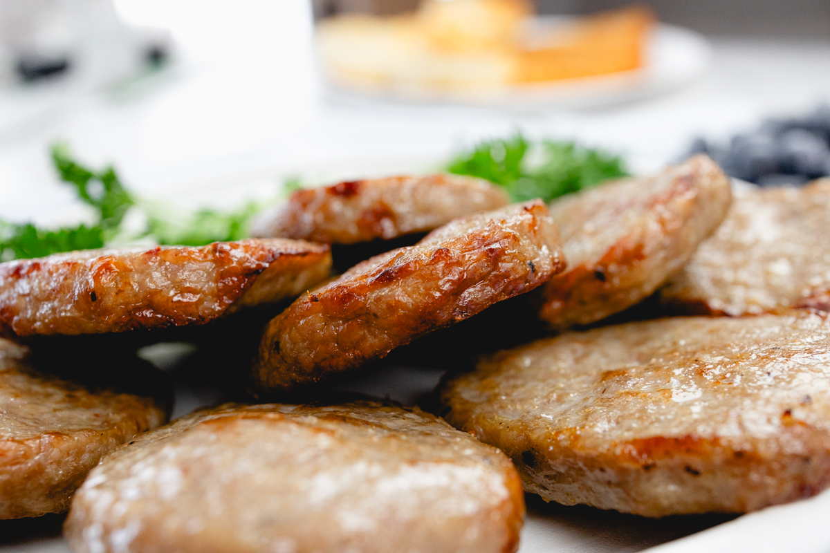 Close up of cooked sausage patties on a white plate with a leafy green garnish to the side.