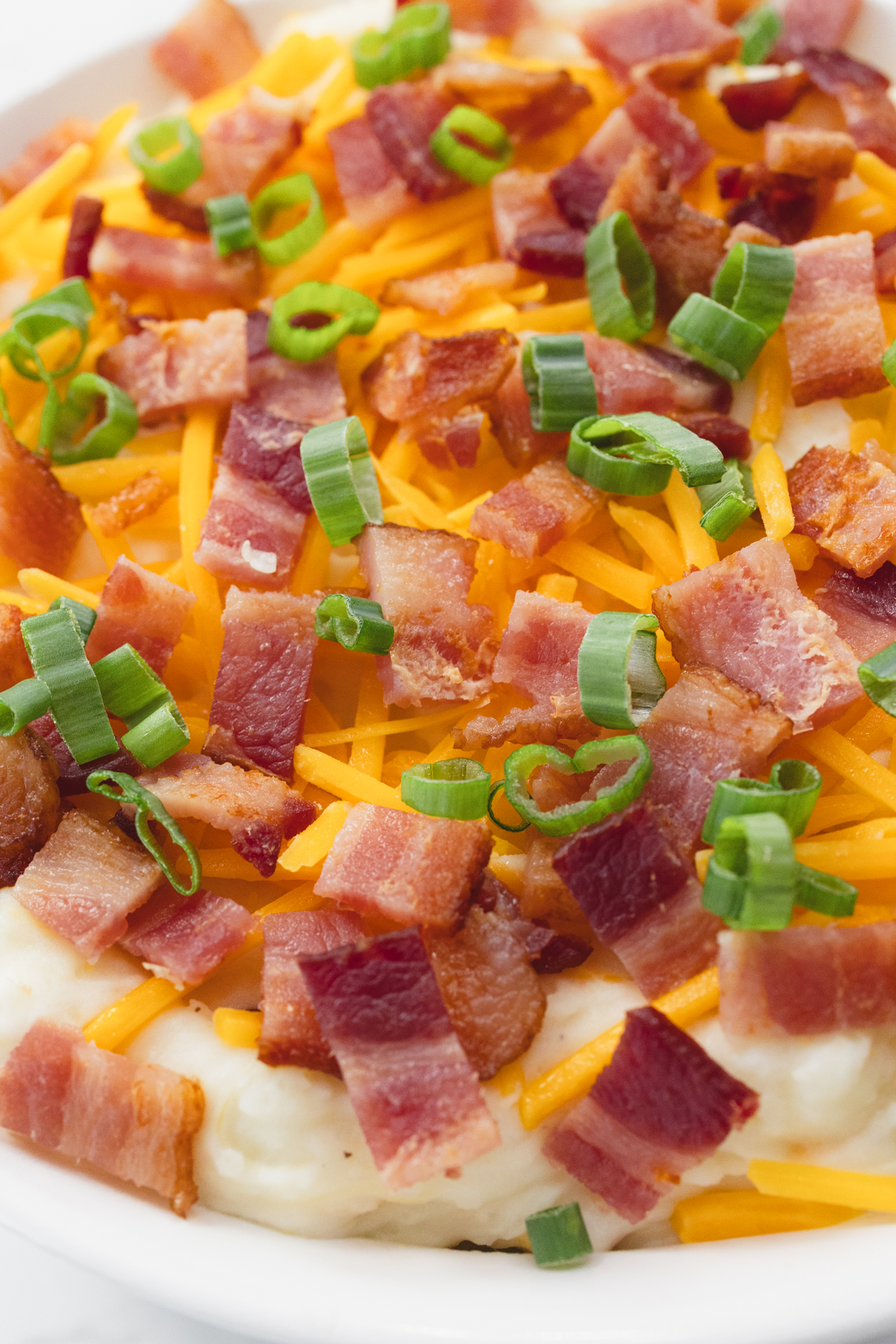 Very close up view of a white dish filled with loaded mashed potatoes.