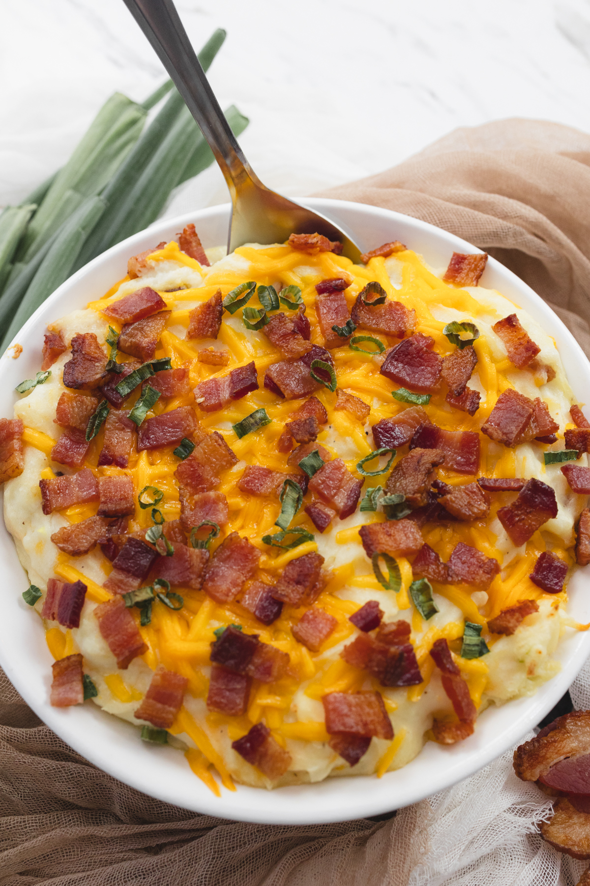 Close up view of a white dish filled with loaded mashed potatoes.