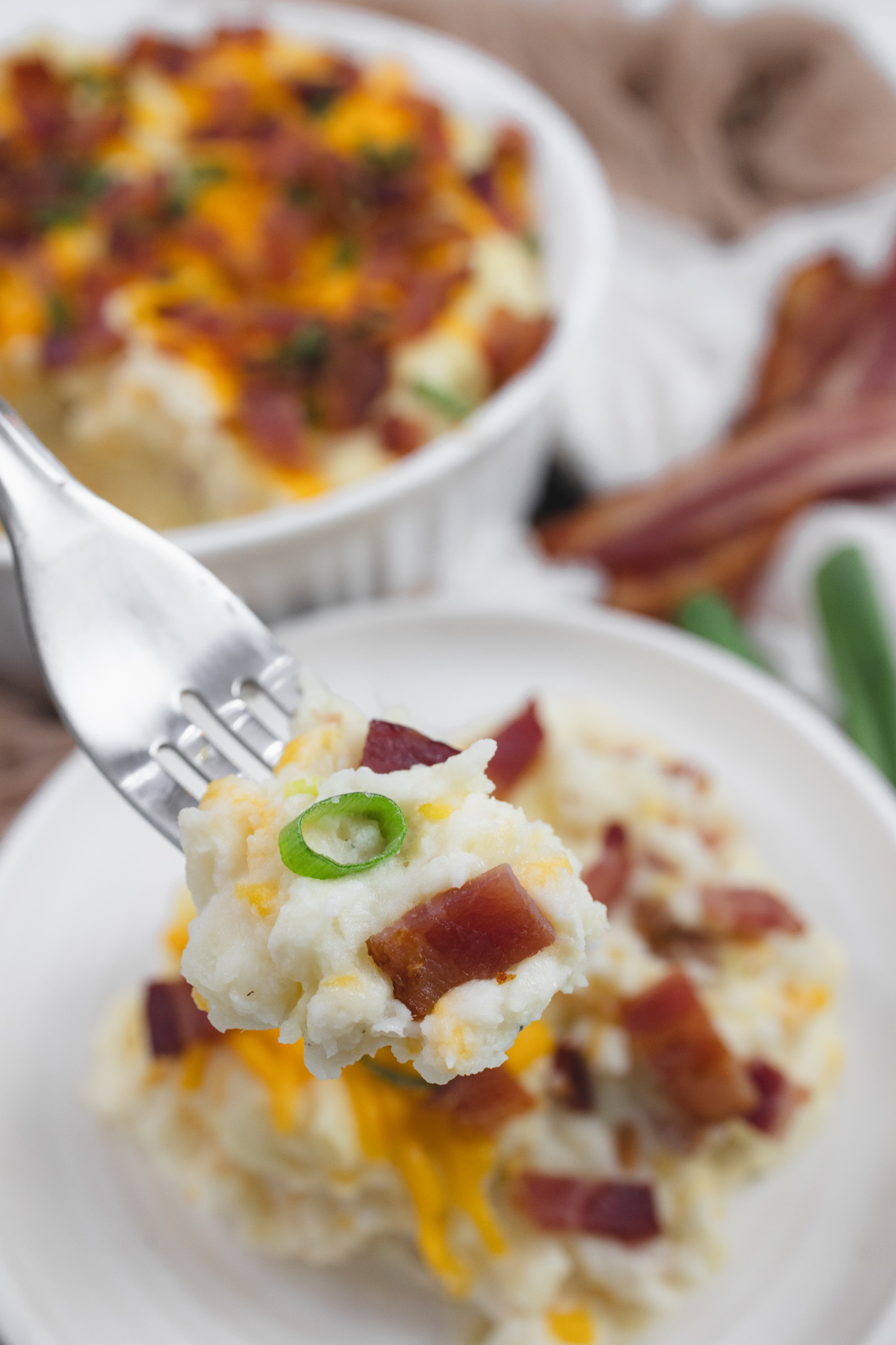 Close up shot of a fork lifting up a bite of loaded mashed potatoes, with the plate in the background.