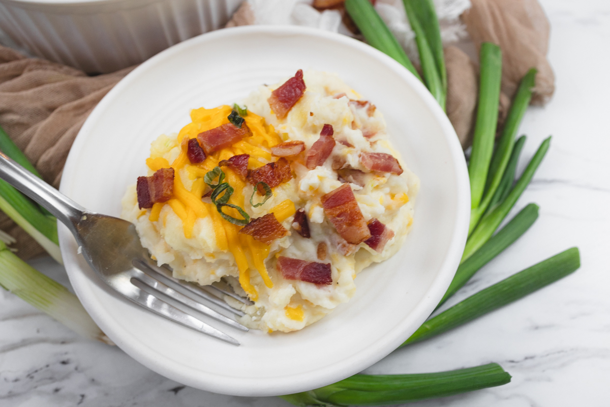 Close up view of a plate with a serving of loaded mashed potatoes on it.