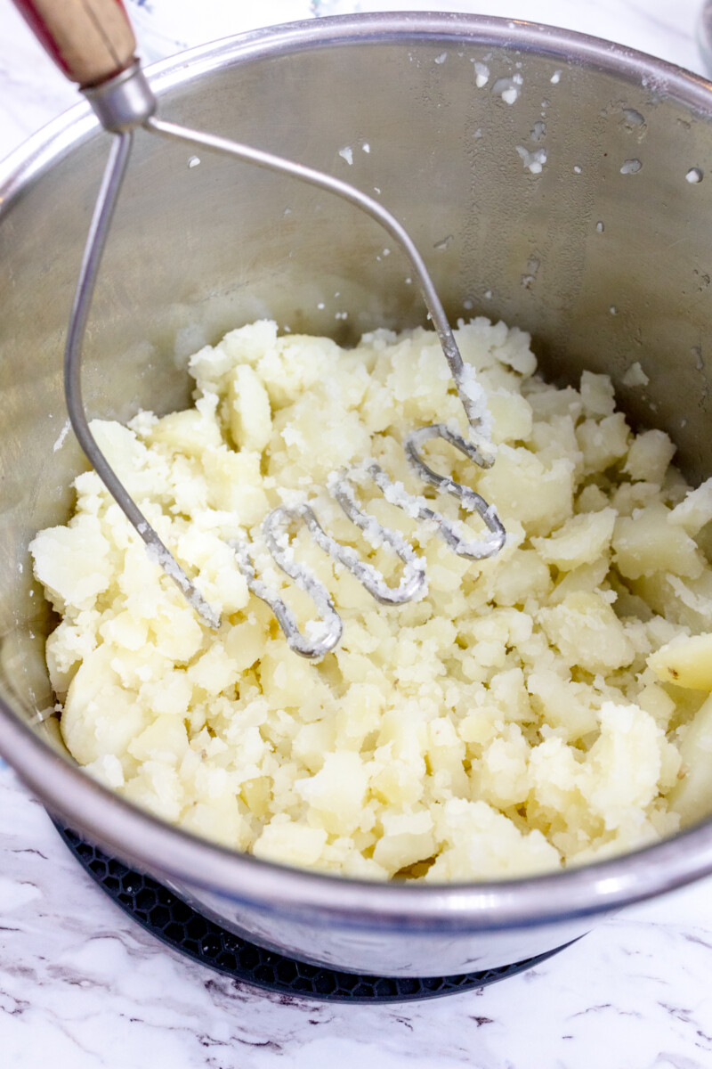 Close image of a potato masher mashing potatoes in an Instant Pot.