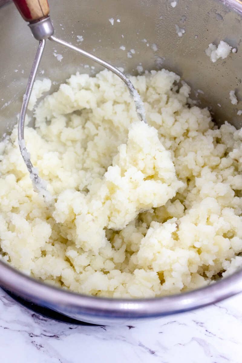 Close image of a potato masher mashing potatoes in an Instant Pot.