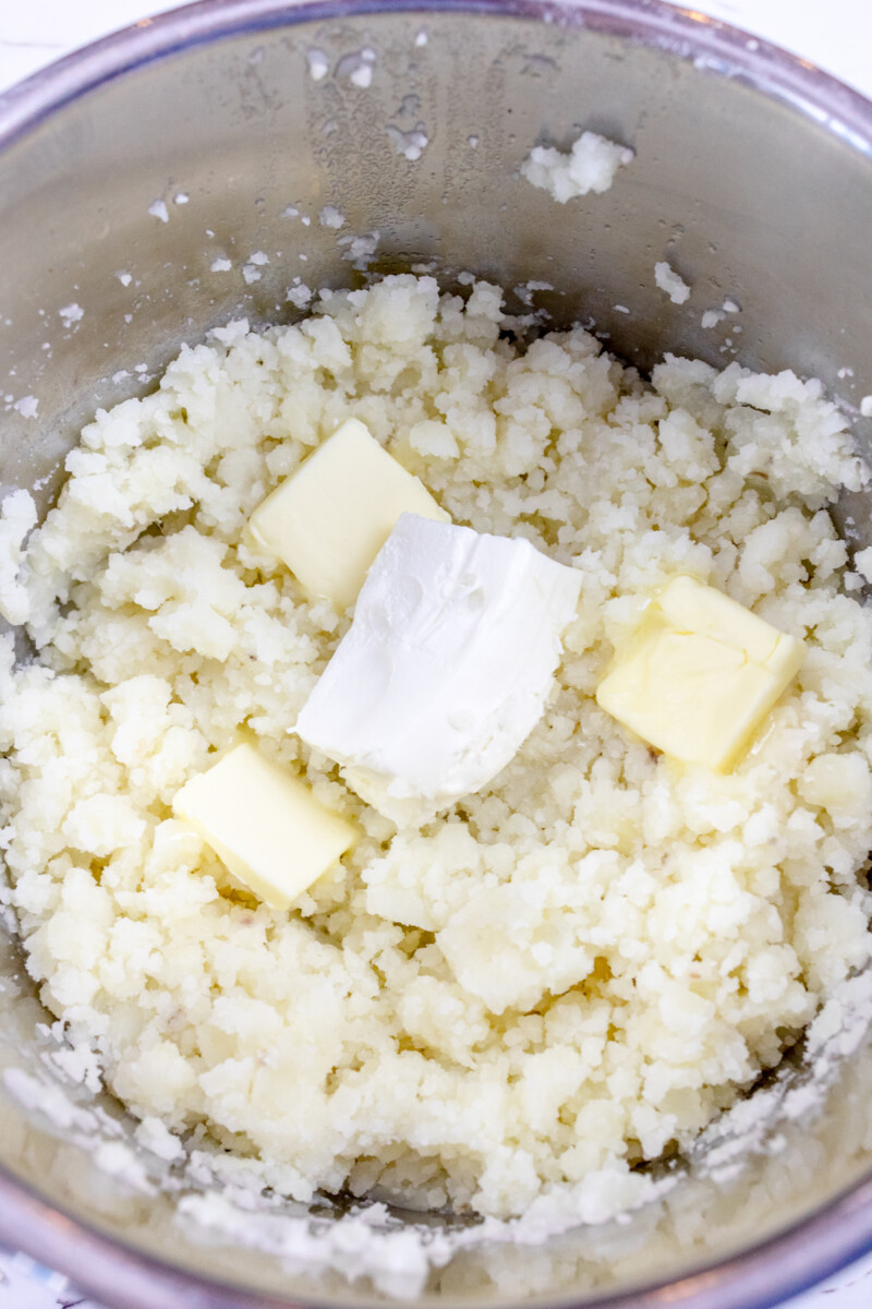 Close image of potatoes in an Instant Pot with butter and cream cheese added but not yet mixed in.