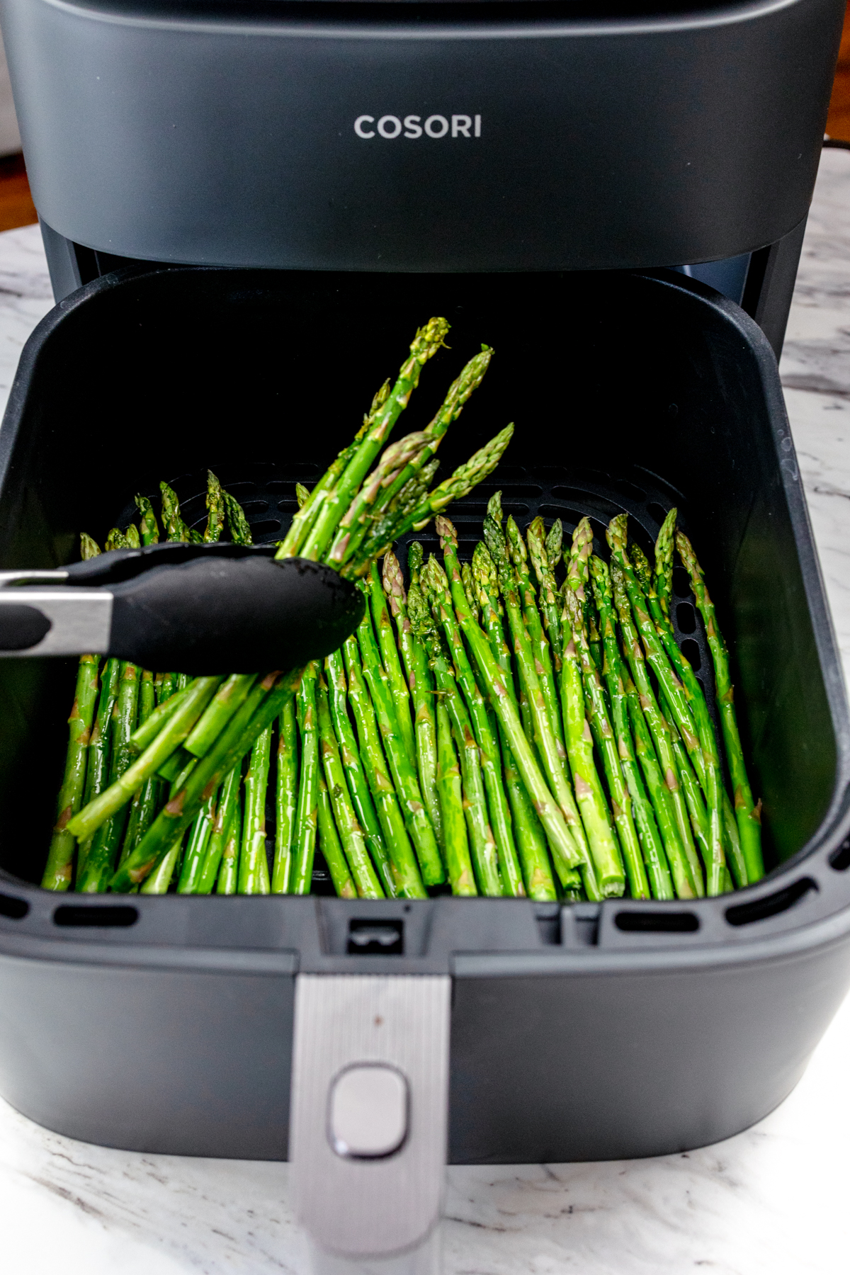 A close up shot of tongs handling asparagus in the Air Fryer.