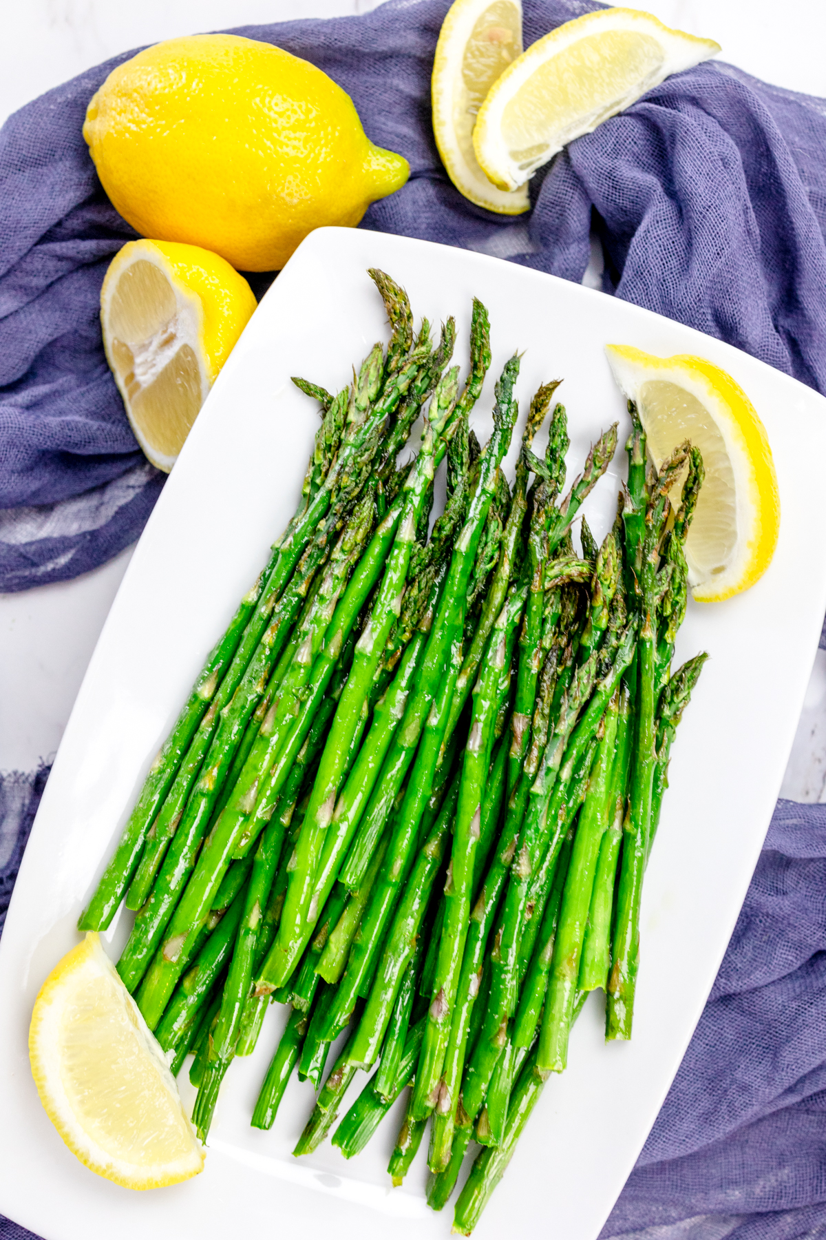 Close up shot of Air Fryer Asparagus on a white plate surrounded by lemons.
