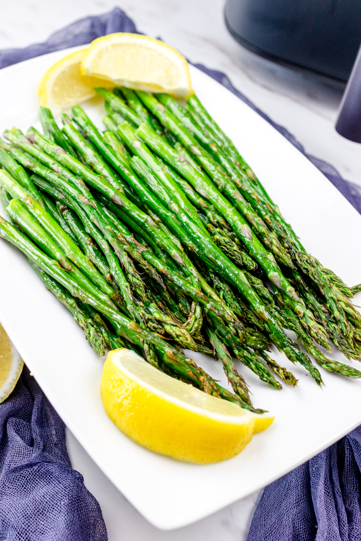 Close up shot of Air Fryer Asparagus on a white plate surrounded by lemons.