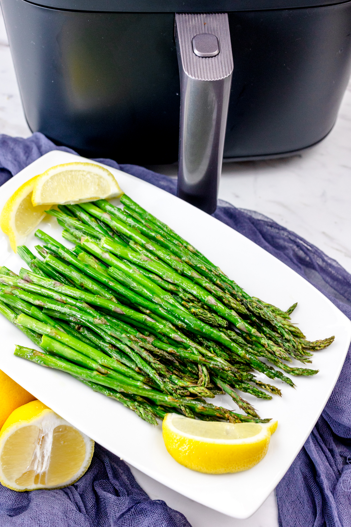Close up shot of Air Fryer Asparagus on a white plate surrounded by lemons.
