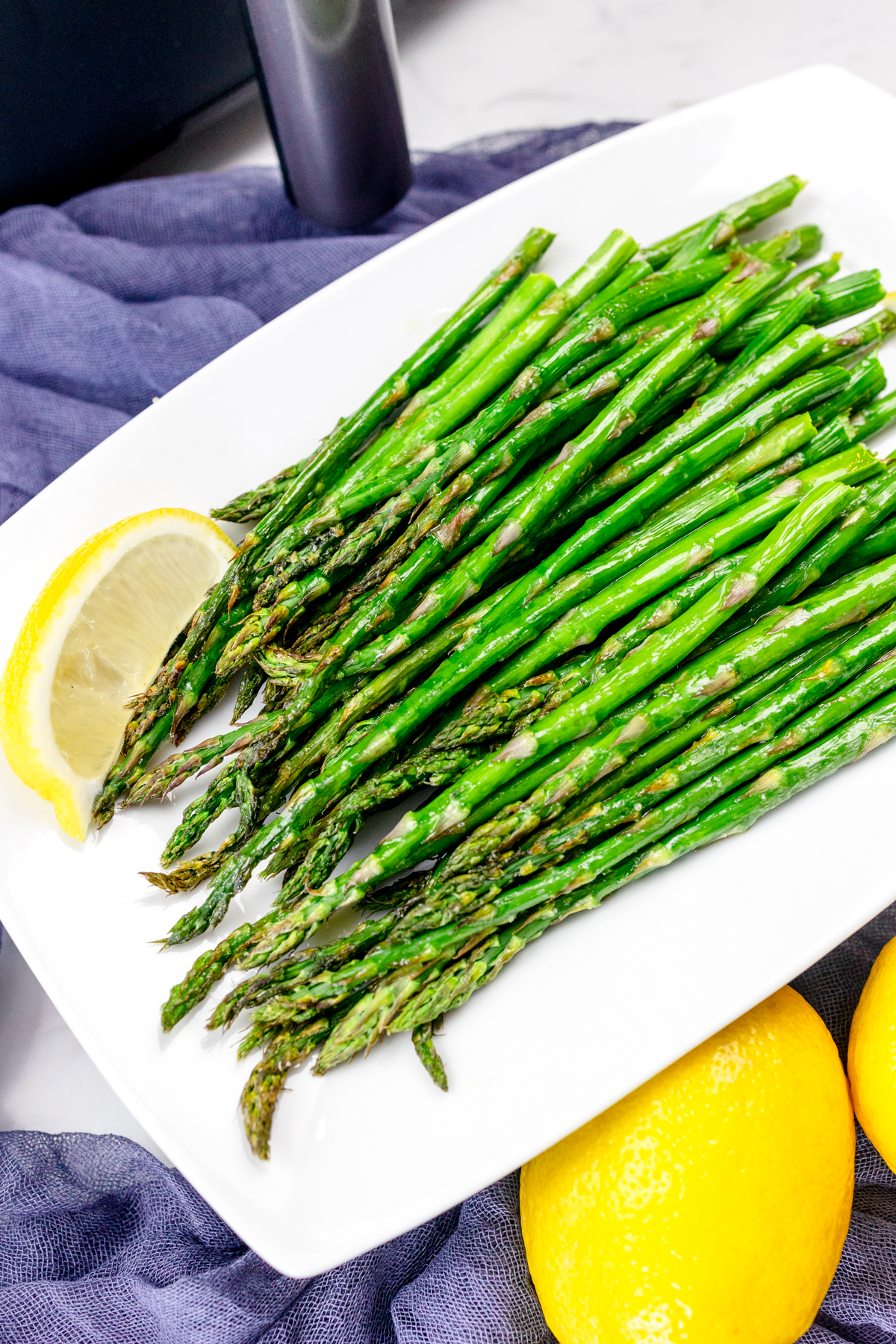 Close up shot of Air Fryer Asparagus on a white plate surrounded by lemons.