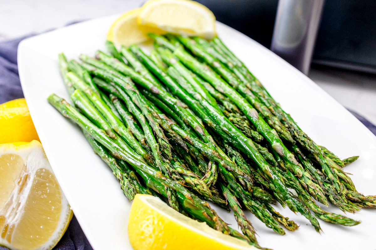 Close up shot of Air Fryer Asparagus on a white plate surrounded by lemons.