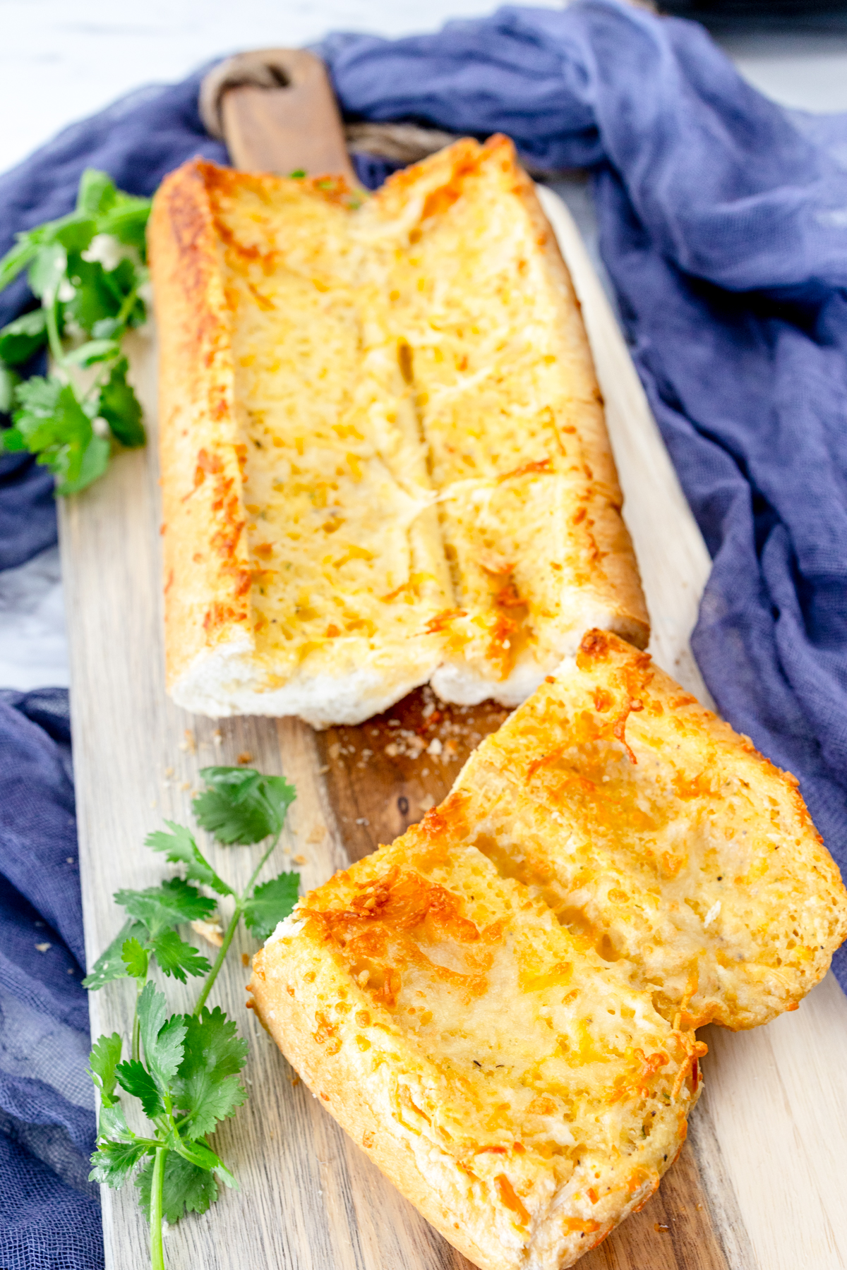 Close up image of air fried garlic bread on a wooden chopping board with fresh parsley around it for decoration.