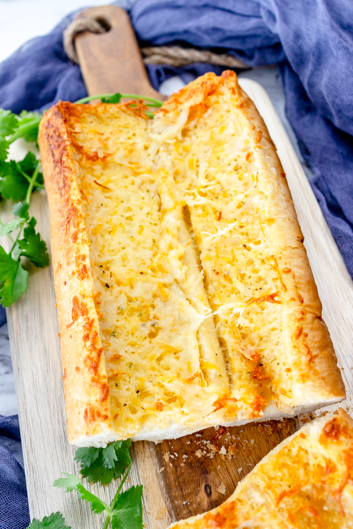 Close up image of air fried garlic bread on a wooden chopping board with fresh parsley around it for decoration.