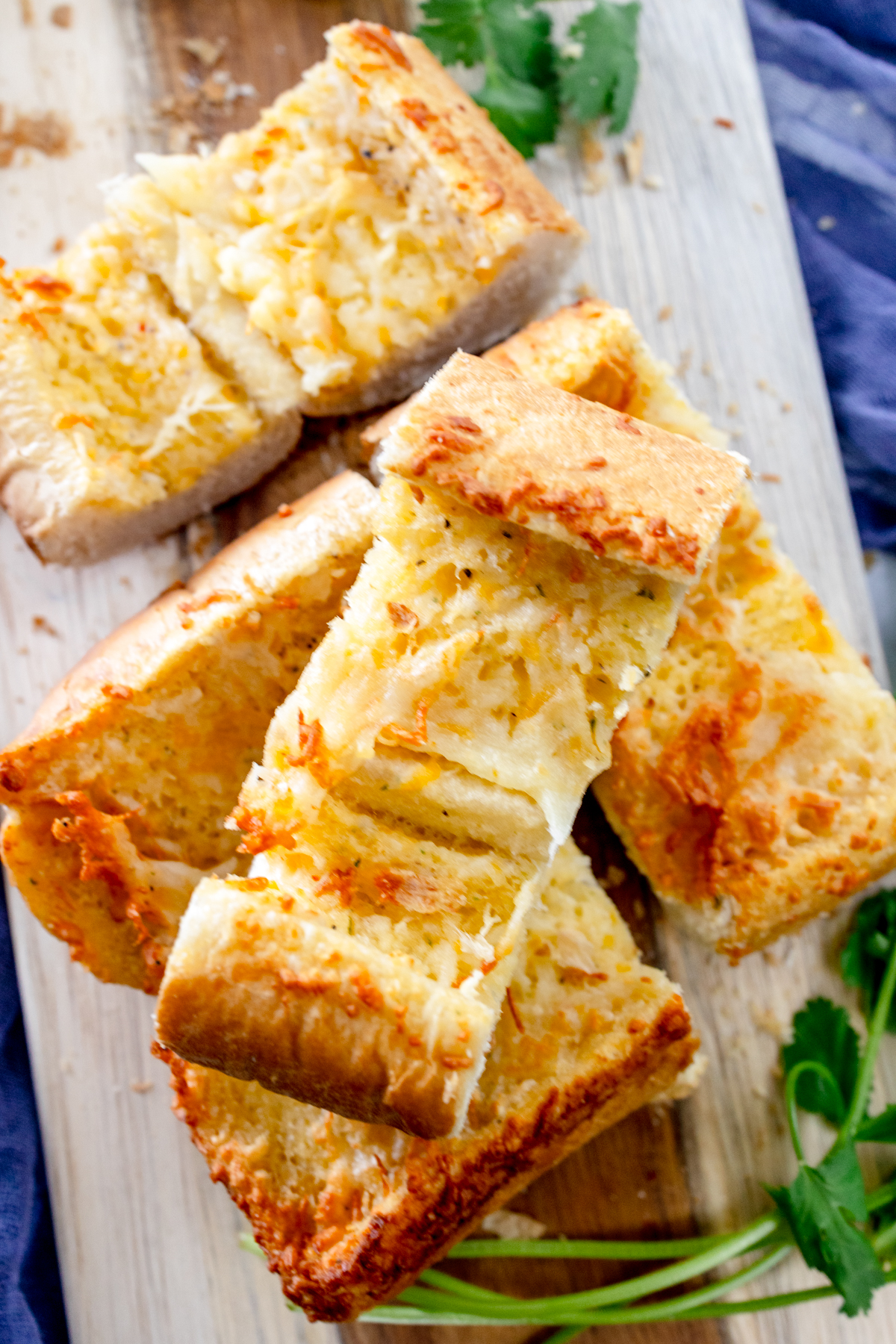 Close up image of air fried garlic bread on a wooden chopping board with fresh parsley around it for decoration.