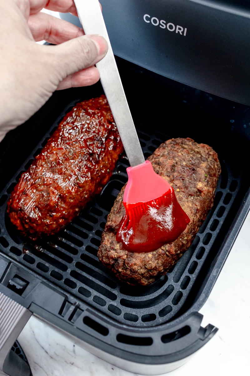 Close up view of homemade meatloaf in the air fryer being brushed with sauce.