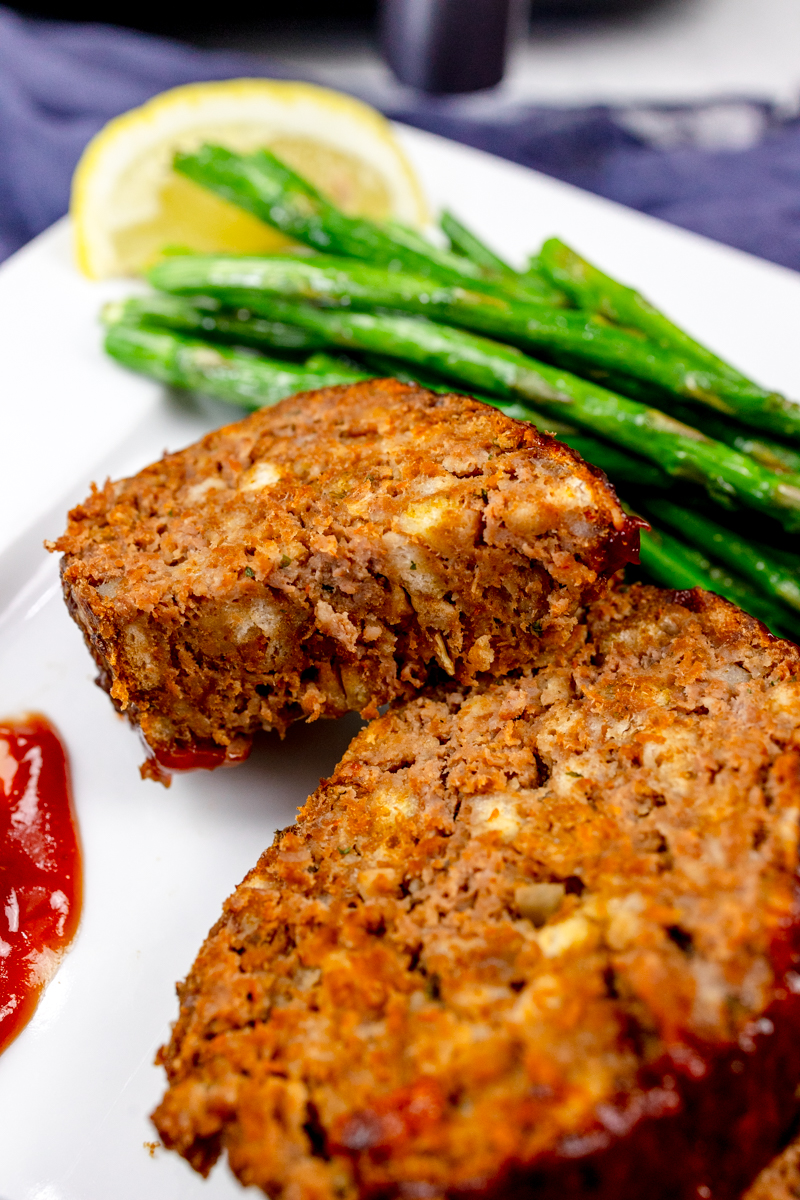 Close view of meatloaf slices on a white plate with asparagus and dipping sauce.