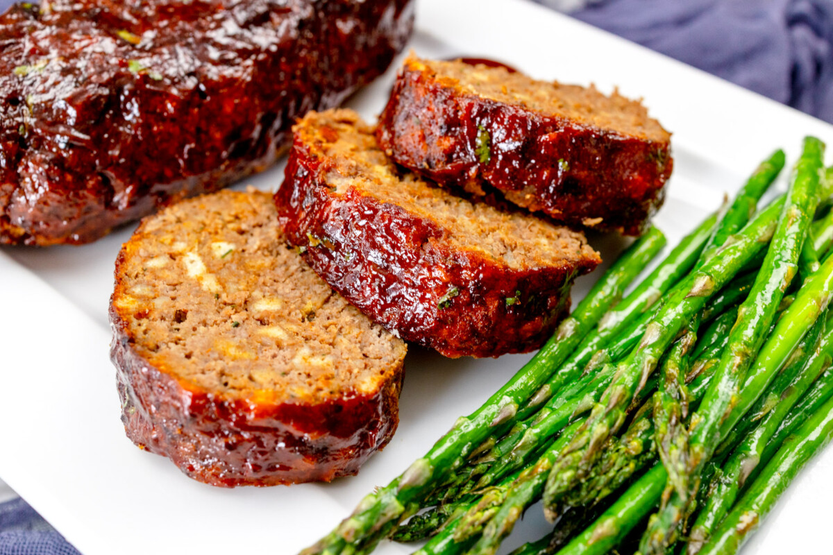 Close view of meatloaf slices on a white plate with asparagus.