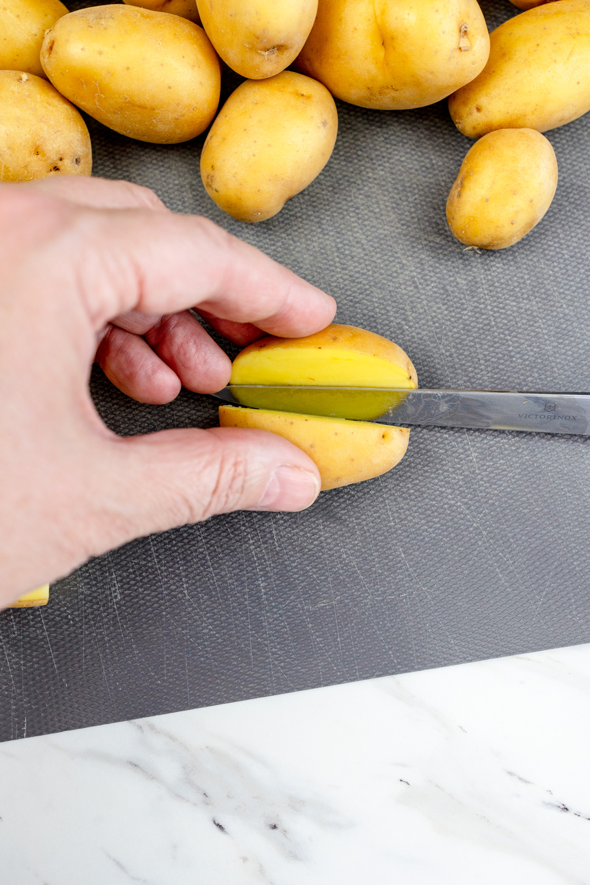 Baby potatoes being sliced lengthwise in half.