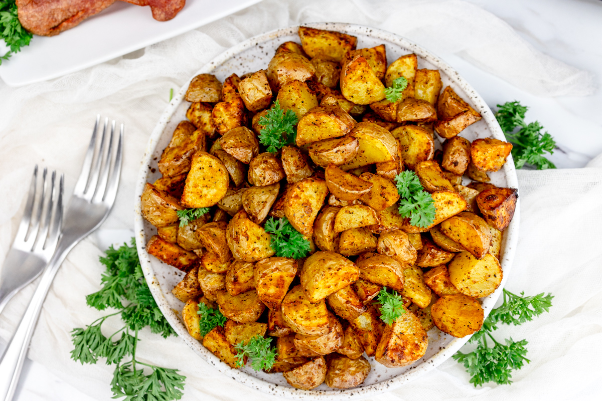 Air Fryer Breakfast Potatoes on a white plate with a leafy green garnish.
