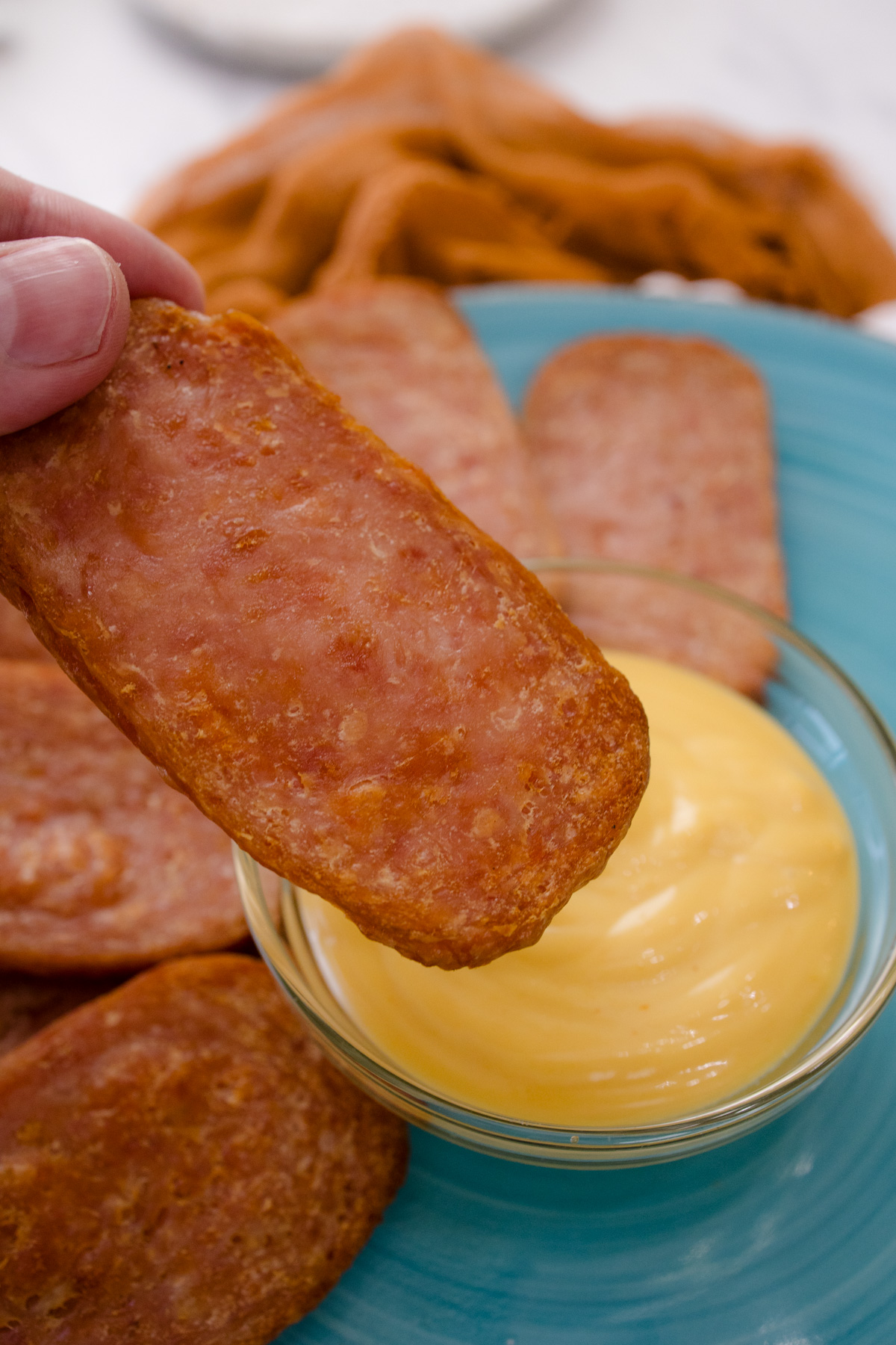 An air fried spam slice being dipped in a small bowl of yellow sauce.
