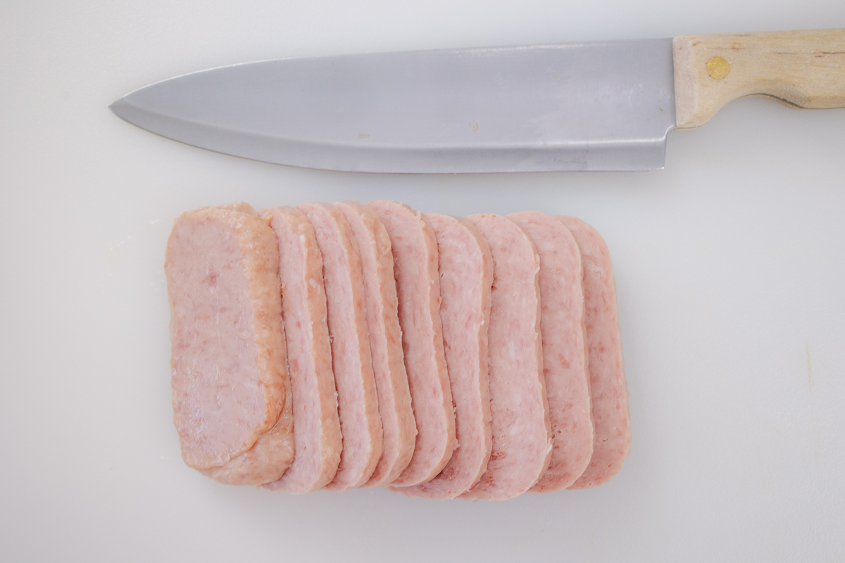 Slices of spam on a white surface next to a sharp knife.