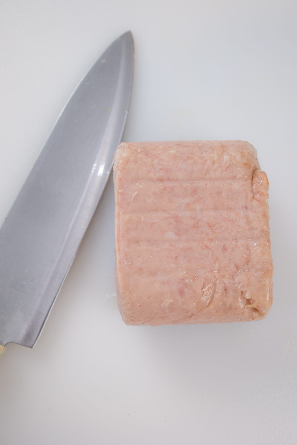 Spam on a white surface next to a sharp knife.
