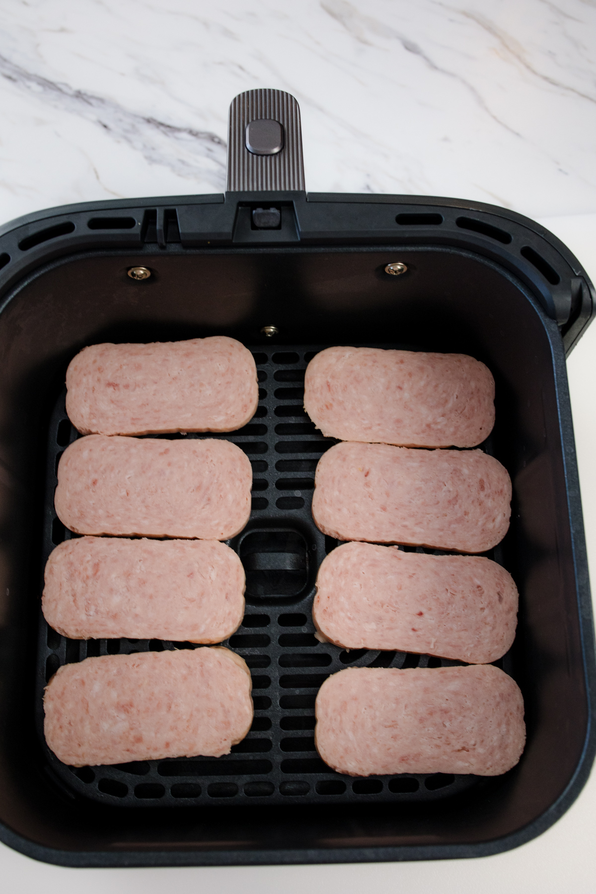 Uncooked sliced spam in an air fryer basket.