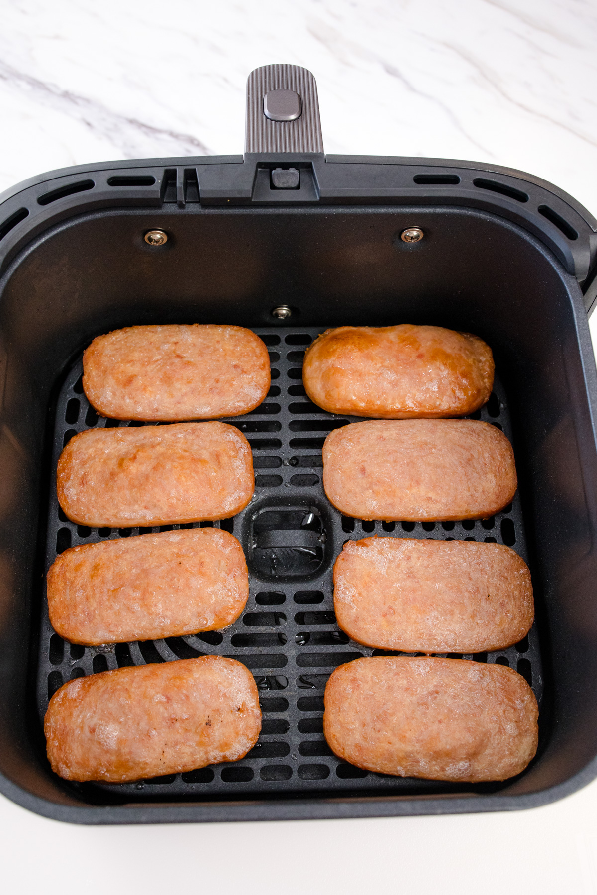 Cooked slices of spam in an air fryer basket.
