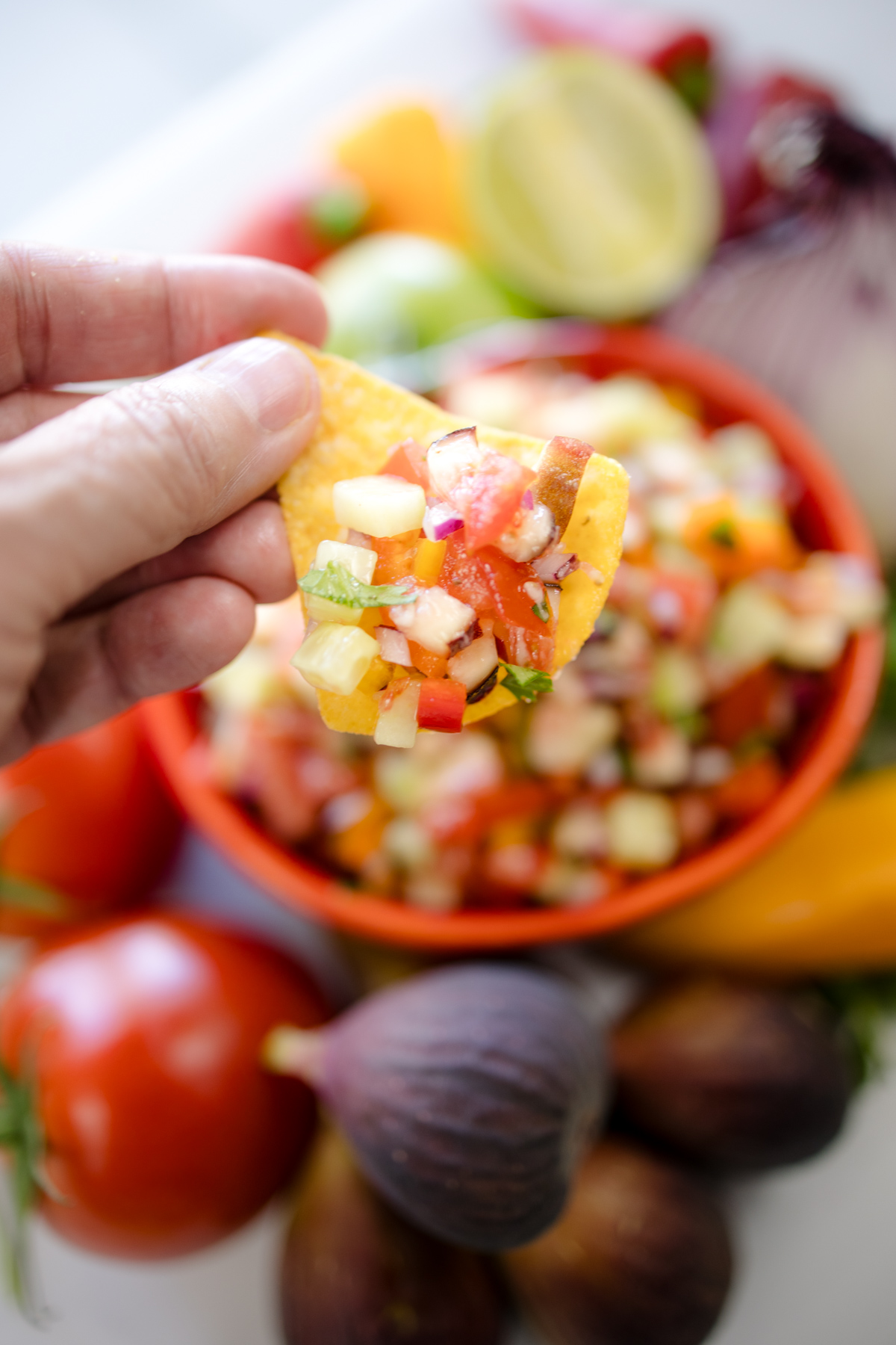 A hand using a tortilla chip to scoop up some Fig Salsa.