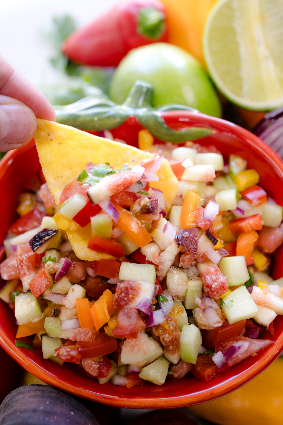A hand using a tortilla chip to scoop up some Fig Salsa.