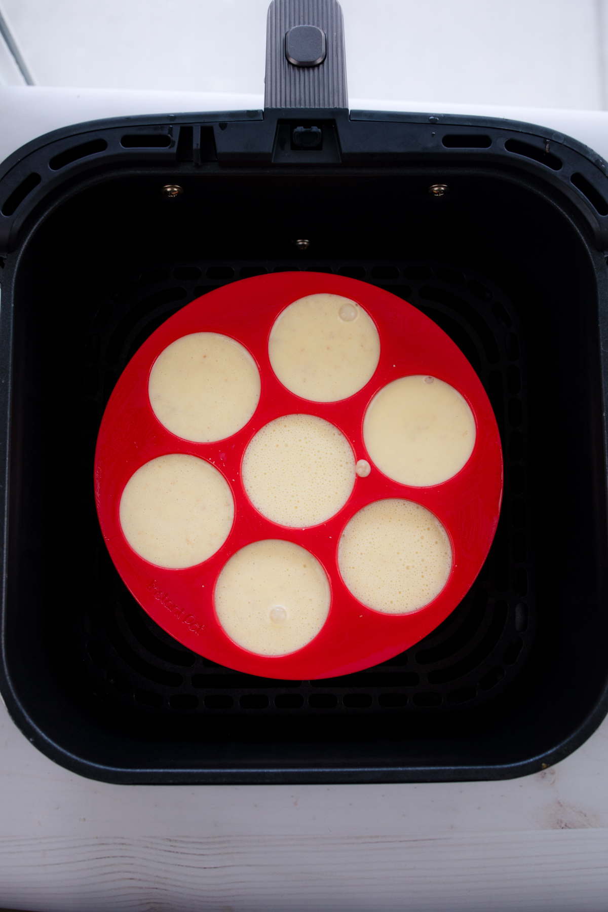 Overhead shot of red silicone dish containing egg bites mixture in air fryer basket.