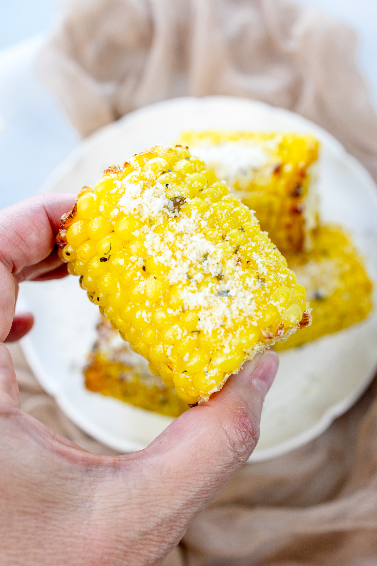 Close up of a hand holding a mini air fried corn on the cob.