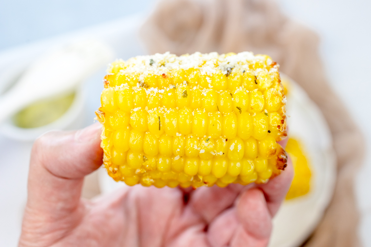 Close up of a hand holding a mini air fried corn on the cob.