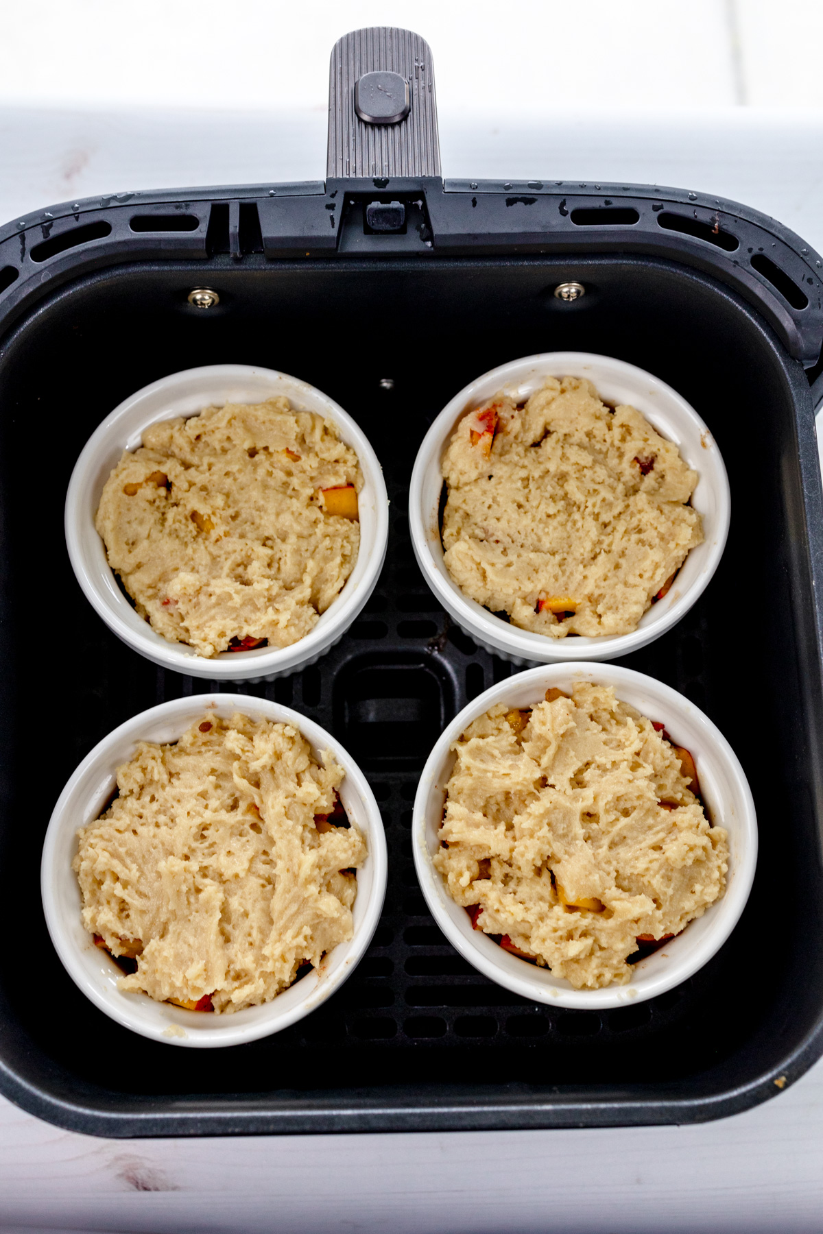 Overhead image of four ramekins of uncooked Peach Cobbler in an air fryer basket.