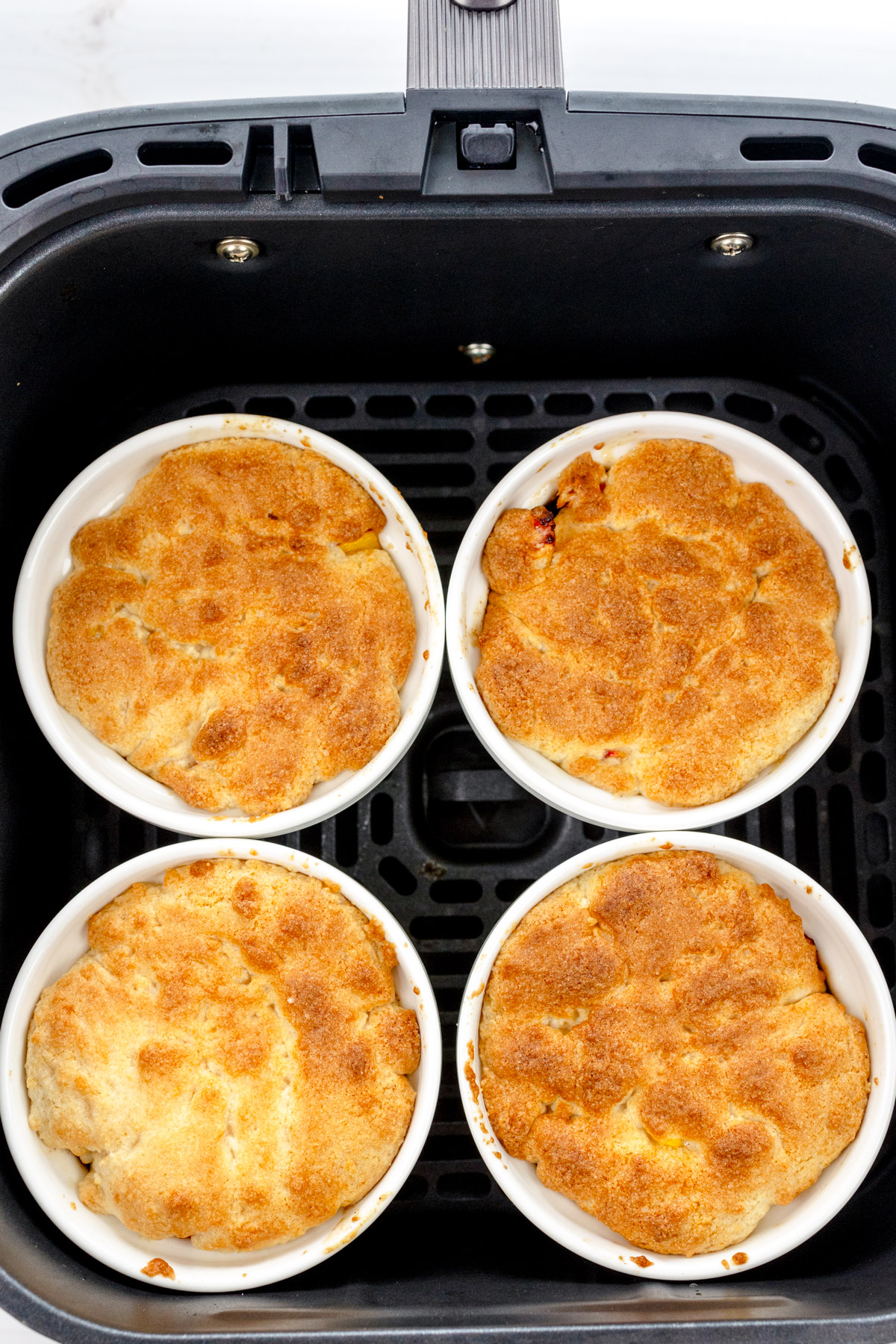 Overhead image of four ramekins of cooked Peach Cobbler in an air fryer basket.