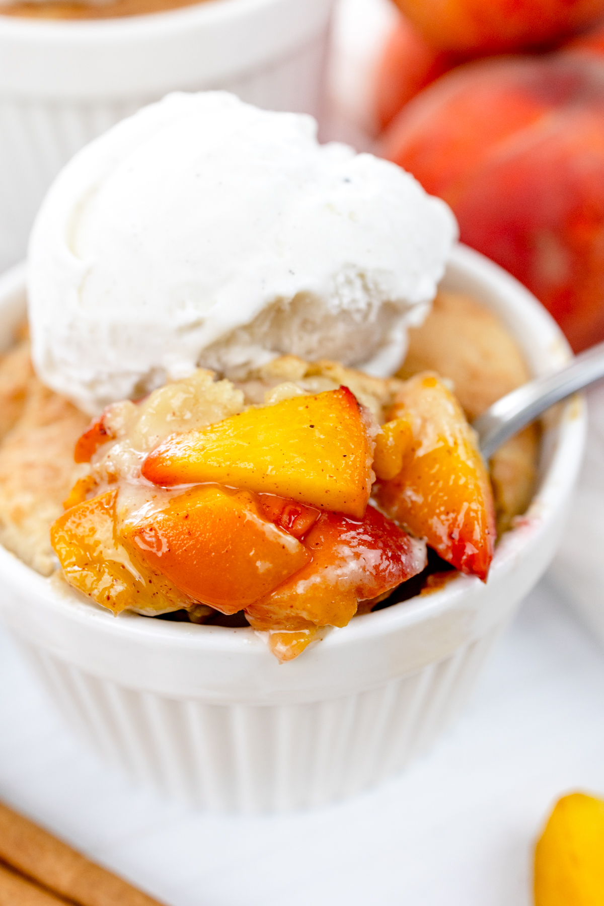 Close up image of Air Fryer Peach Cobbler in a ramekin with whipped cream on top, with peaches and cinnamon sticks around it.