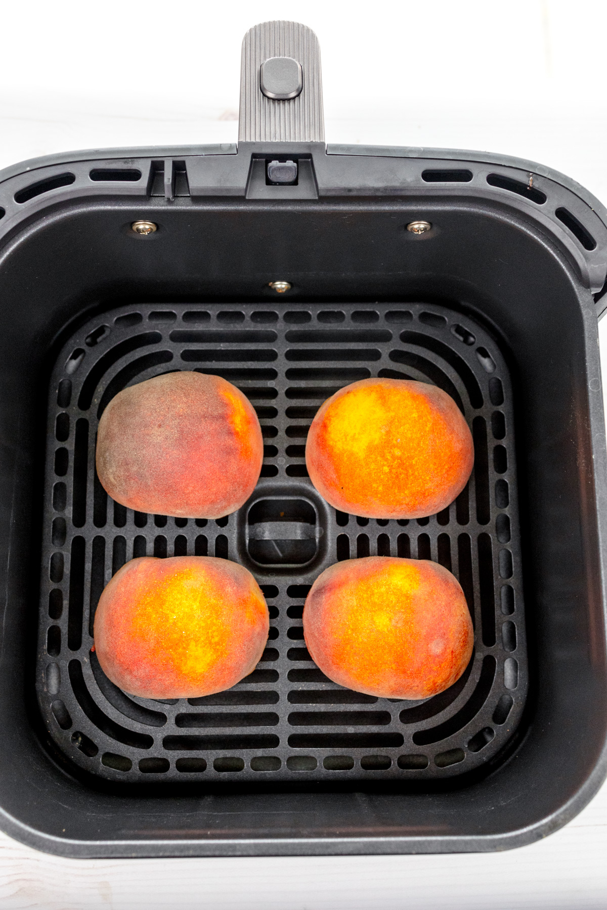 Overhead image of peach halves in an air fryer basket, with the sliced side facing down.