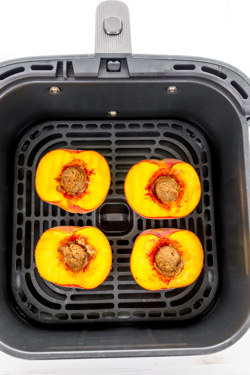 Overhead image of peach halves in an air fryer basket, with the sliced side facing up.