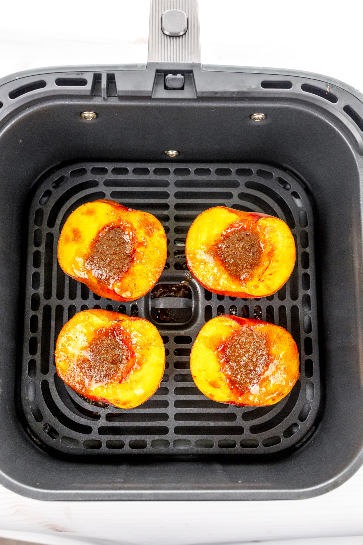 Overhead image of peach halves in an air fryer basket, with the sliced side facing up.