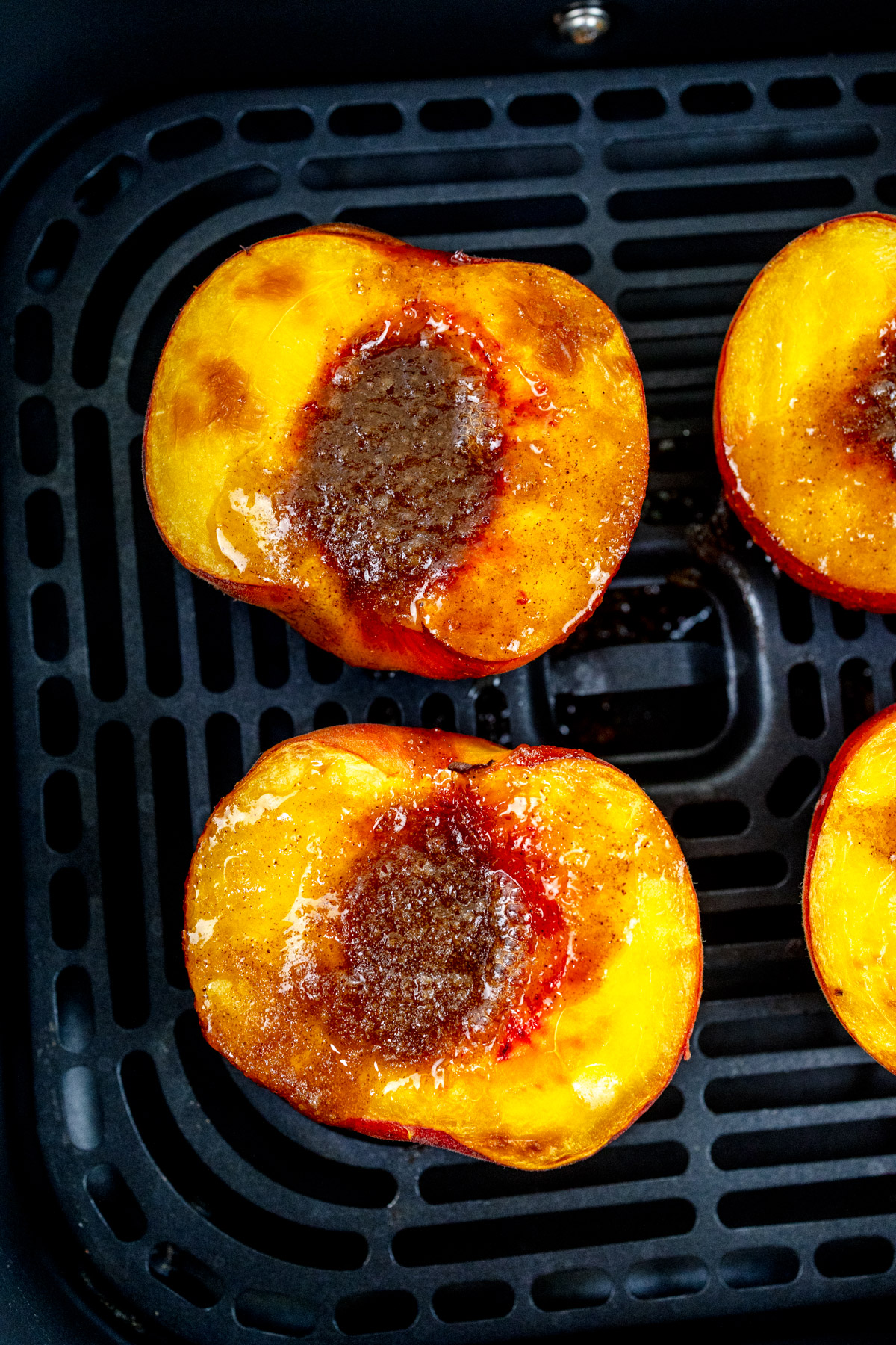 Close up image of peach halves in an air fryer basket, with the sliced side facing up.