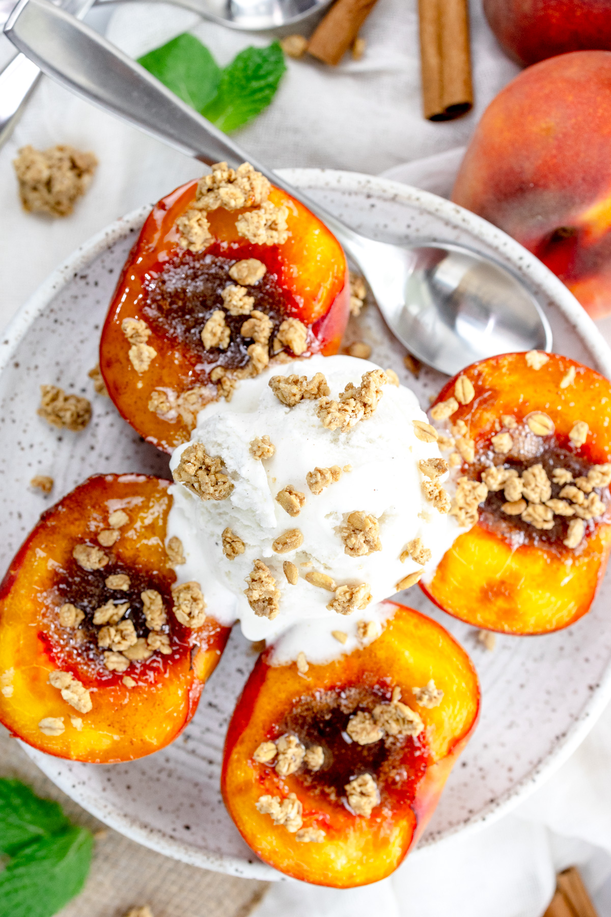 Overhead image of Air Fryer Peaches on a white plate with a scoop of ice cream and crumb sprinkling on top, and a spoon.
